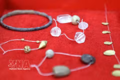 Glass beads, gold-coloured metal beads and leaf-shaped objects uncovered in the tombs. (Photo: VNA)