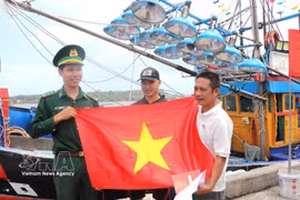 Fishermen receive national flag from a border officer (Photo: VNA)