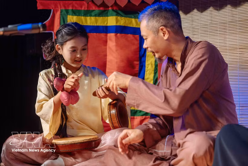 A young girl enjoys learning about musical instruments from an artisan. (Photo: VNA)