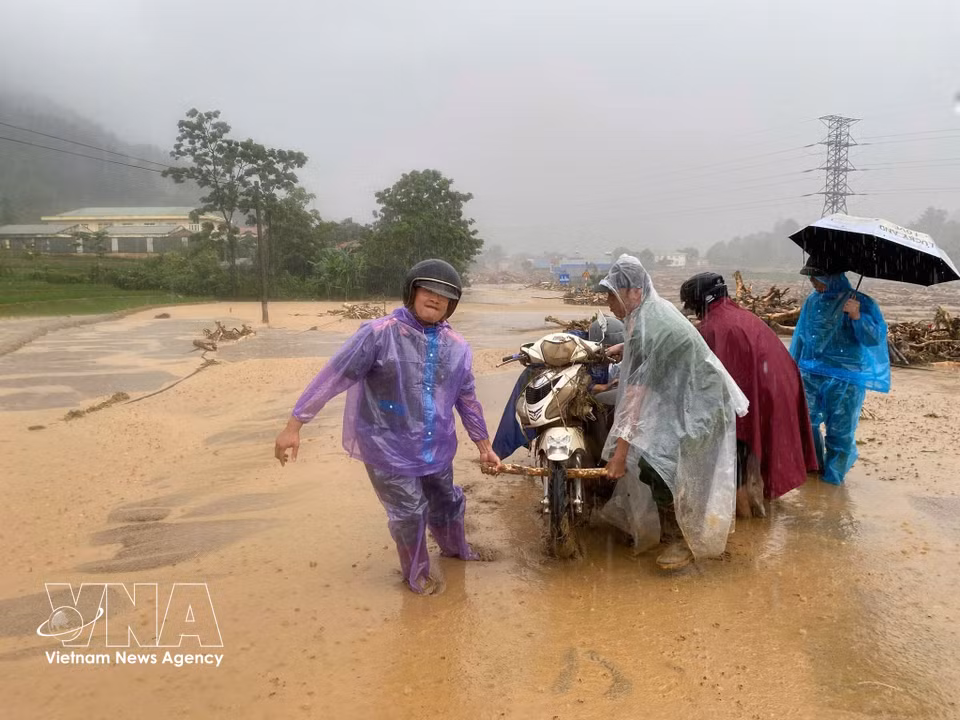 Residents wade through mud to move motorbikes away from the landslide site. (Photo: VNA)