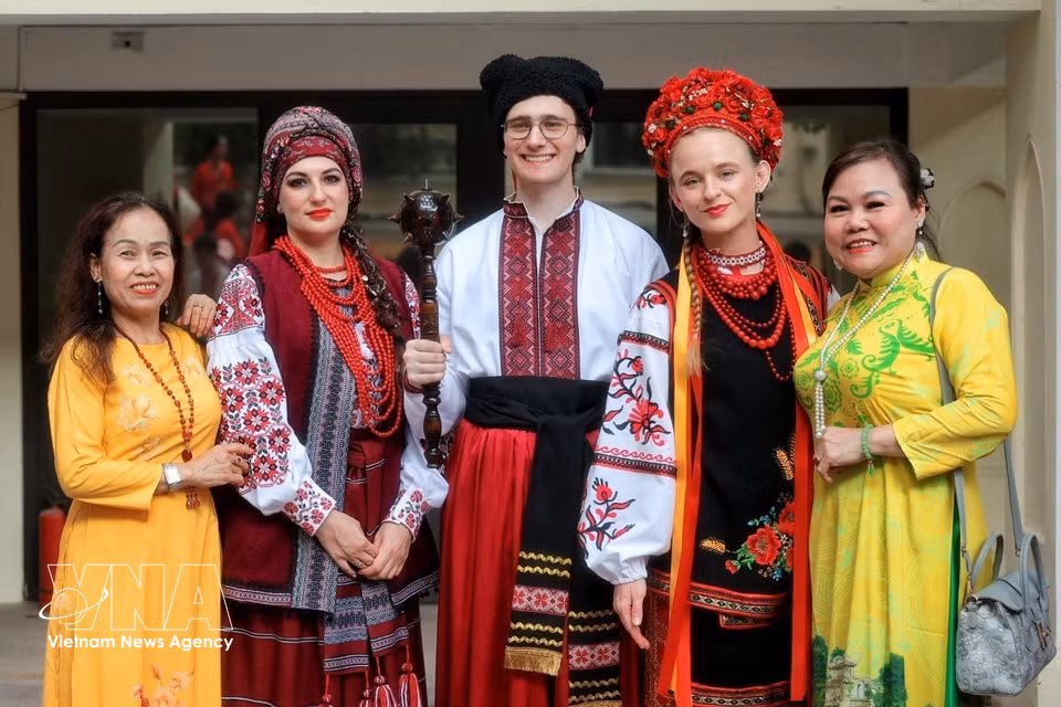 Members of international delegations in traditional costumes pose for photos with Vietnamese people. (Photo: VNA)