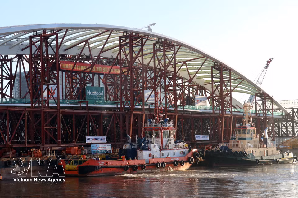 Tugboats gradually manoeuvre the main span into position between the two completed sections of the bridge. (Photo: VNA)