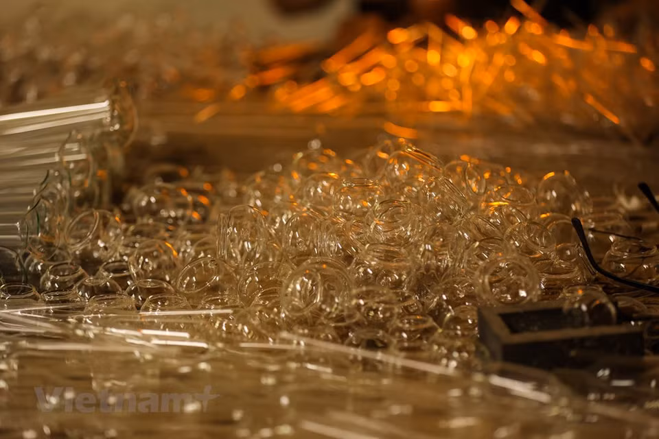 A skillful glass-blower needs to know the ‘ripeness’ of glass. As glass is initially exposed to fire, it will appear blue in color before turning white. At that time, a slight blow is enough to mold the blob of molten glass into products of their desired shape, according to the professional glass-smith Le Xuan Tien. The glass-blowing technique plays a crucial role in creating products. A glass blower has to hold his breath properly to produce specific products. From basic tools, residents in Thong Nhat commune, Thuong Tin district, the capital city of Hanoi could produce simple and useful glassware like light bulbs, bottles, vases, vacuum flask stoppers or any other delicate products according to customers’ demands. (Photo: VietnamPlus)