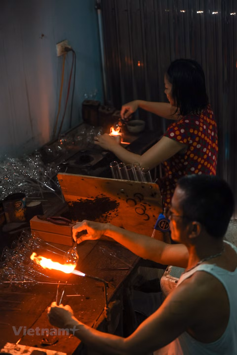 Along with traditional glass products, many households in Thong Nhat commune have won contracts to supply glass items for education and healthcare establishments. In order to make good products, the glassblowers should know glass very well. When glass is put into fire, it is green; when molten glass turns transparent, it is ready to be blown. Then, glassblowers just need to slightly blow to introduce air to the molten blob of glass to make it expand into desired shapes. The glass-blowing technique plays a crucial role in creating products. A glass-blower has to hold his breath properly to produce specific products. A skillful glass-blower needs to know the ‘ripeness’ of glass. (Photo: VietnamPlus)