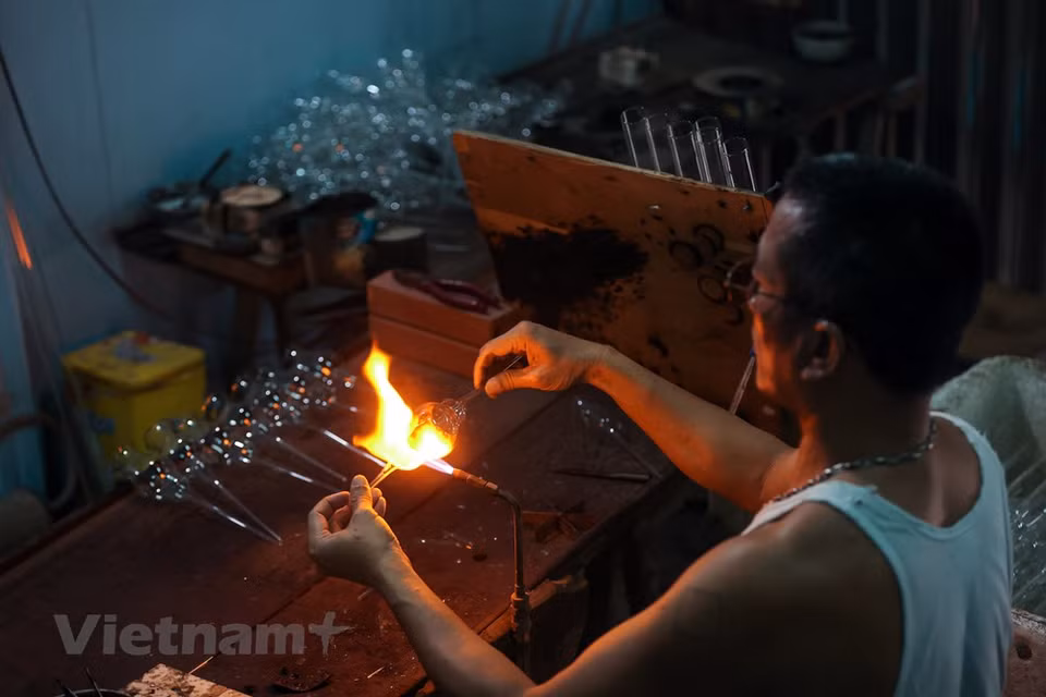 Ho Quang Hien, a professional glass-smith with more than 34 years of experience, said that besides simple items, his workshop is able to make complex products. In a bid to make sound items, Hien has to work in an extremely harsh condition with temperature of the torch lighter reaching over 700 degrees Celsius. Glass blowers in Hoang Xa village, Thong Nhat commune, Thuong Tin district spend days skillfully blowing air through one end of a long glass pipe in order to create various pieces for their customers. They refuse to let their swollen, blistered mouth stand in the way of their passion. (Photo: VietnamPlus)