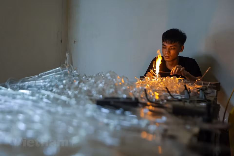 Le Duy Dai, born in 2000, is working at Le Xuan Tien’s workshop. He is working diligently to make glass products. Glass-blower Le Xuan Tien and his workers do not let the brutal temperatures blanketing the Vietnamese capital keep them from turning out beautiful pieces of art in their 20-square-meter workshop in Hoang Xa Village, Thong Nhat Commune, Thuong Tin District. Tien and his workers spend days skillfully blowing air through one end of a long glass pipe in order to create various pieces for his customers. They refuse to let their swollen, blistered mouths stand in the way of their passion. (Photo: VietnamPlus)