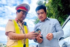 A traffic police officer helps a driver integrate their driving licence and vehicle documents to the VNeID app. (Photo: VNA)