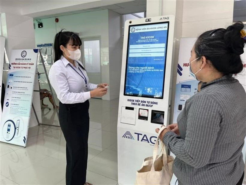 Long An General Hospital's staff guides a local resident on how to use the self-service medical check-in kiosk. (Photo: VNA)