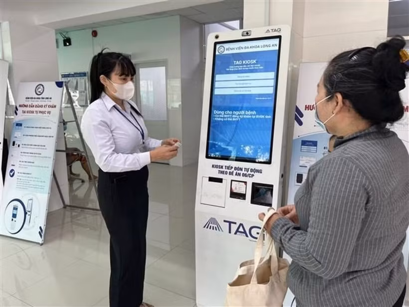 Long An General Hospital's staff guides a local resident on how to use the self-service medical check-in kiosk. (Photo: VNA)
