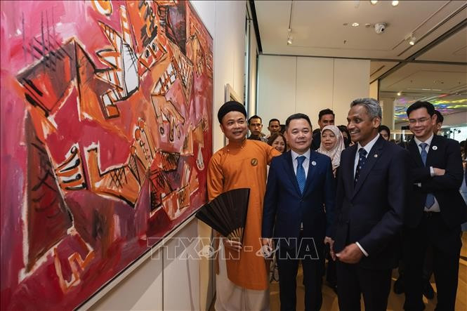 Vietnamese artist Nguyen Tuan Son (left) tell visitors about his paintings at the exhibition. (Photo: VNA) 