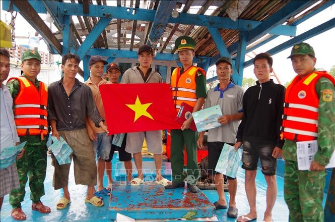 Officers of the Vam Lang border guard station in Dong Thap disseminate information on the prevention of illegal, unreported and unregulated (IUU) fishing and present a national flag to members of a local ship. (Photo: VNA)