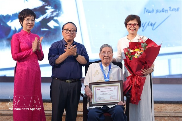 From left, Vietnam News Agency General Director Vu Viet Trang and Jury Chairman, poet Tran Dang Khoa congratulate "Cricket Knight" songwriter Pham Tuyen and his daughter, Pham Hong Tuyen, at the De Men Awards ceremony in Hanoi on May 28, 2025. (Photo: VNA)