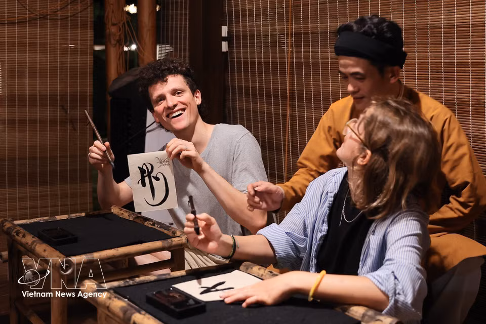 Foreign visitors enjoy trying Vietnamese calligraphy at the Temple of Literature. (Photo: Pham Tuan Anh/VNA)