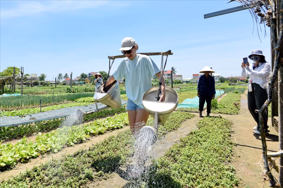 Carrying two water buckets with a yoke on their shoulders proves to be a challenging yet interesting experience for foreign tourists. (Photo: Thanh Hoa/VNA)