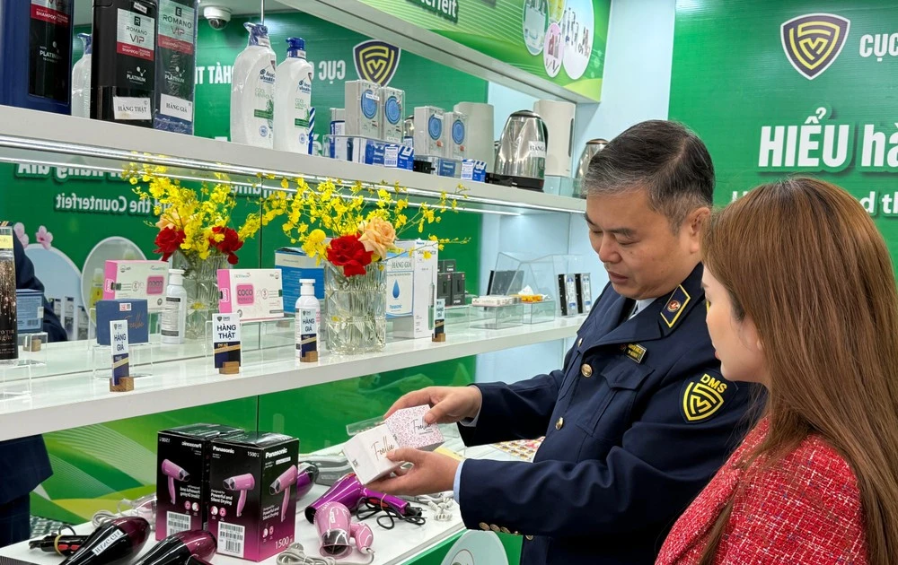 A market surveillance official guides a consumer on how to distinguish between genuine and counterfeit cosmetics. (Photo: VNA)