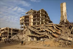 People walking alongside buildings destroyed by conflict in Gaza city (Photo: Xinhua/VNA)