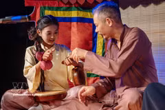 A young girl enjoys learning about musical instruments from an artisan. (Photo: VNA)