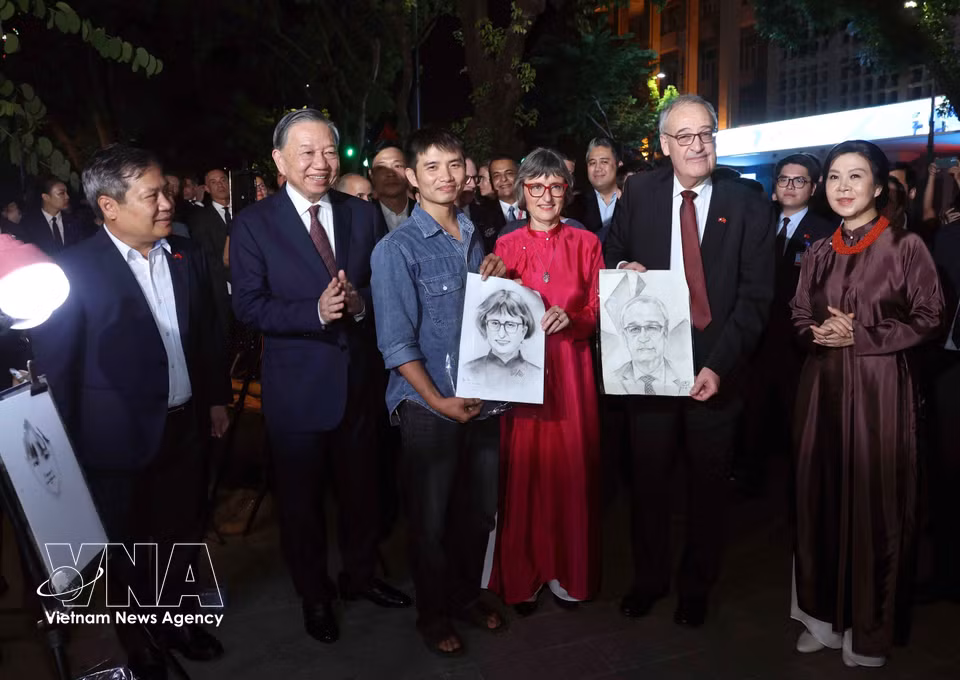 A street artist presents Swiss President Guy Parmelin and his spouse, Caroline Parmelin, with two portrait sketches. (Photo: Thong Nhat/VNA)