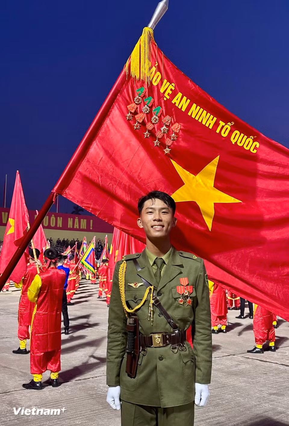 A young soldier’s beaming face besides the national flag (Photo: VietnamPlus)